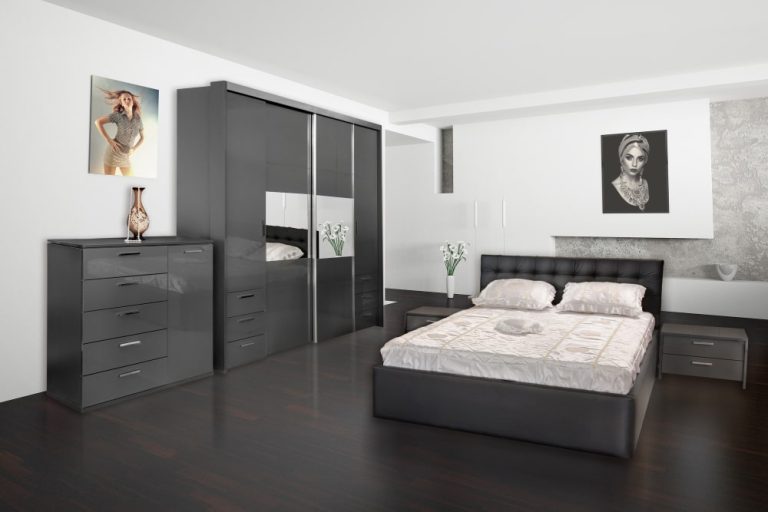 A cozy bedroom featuring a neatly made bed, a wooden dresser, and a wall-mounted mirror reflecting the room's decor.